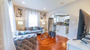 A modern living room with a tufted sofa, a glass coffee table, and a flat-screen TV. - Faboulous and Cozy Apartment in Montclair, NJ (Montclair)