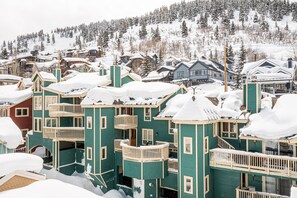 A multi-story building with balconies, surrounded by snow-covered trees and a mountainous backdrop.