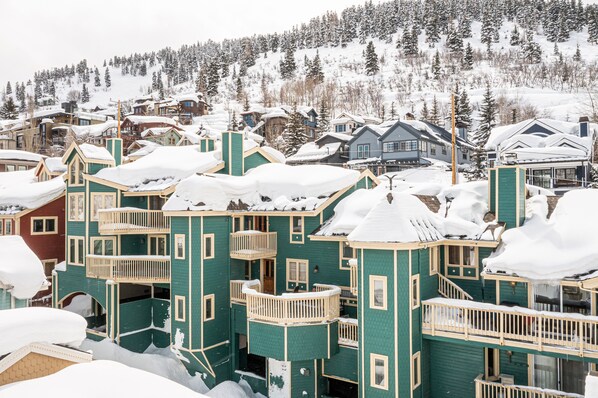 Un edificio de varios pisos con balcones, rodeado de árboles cubiertos de nieve y montañas al fondo.