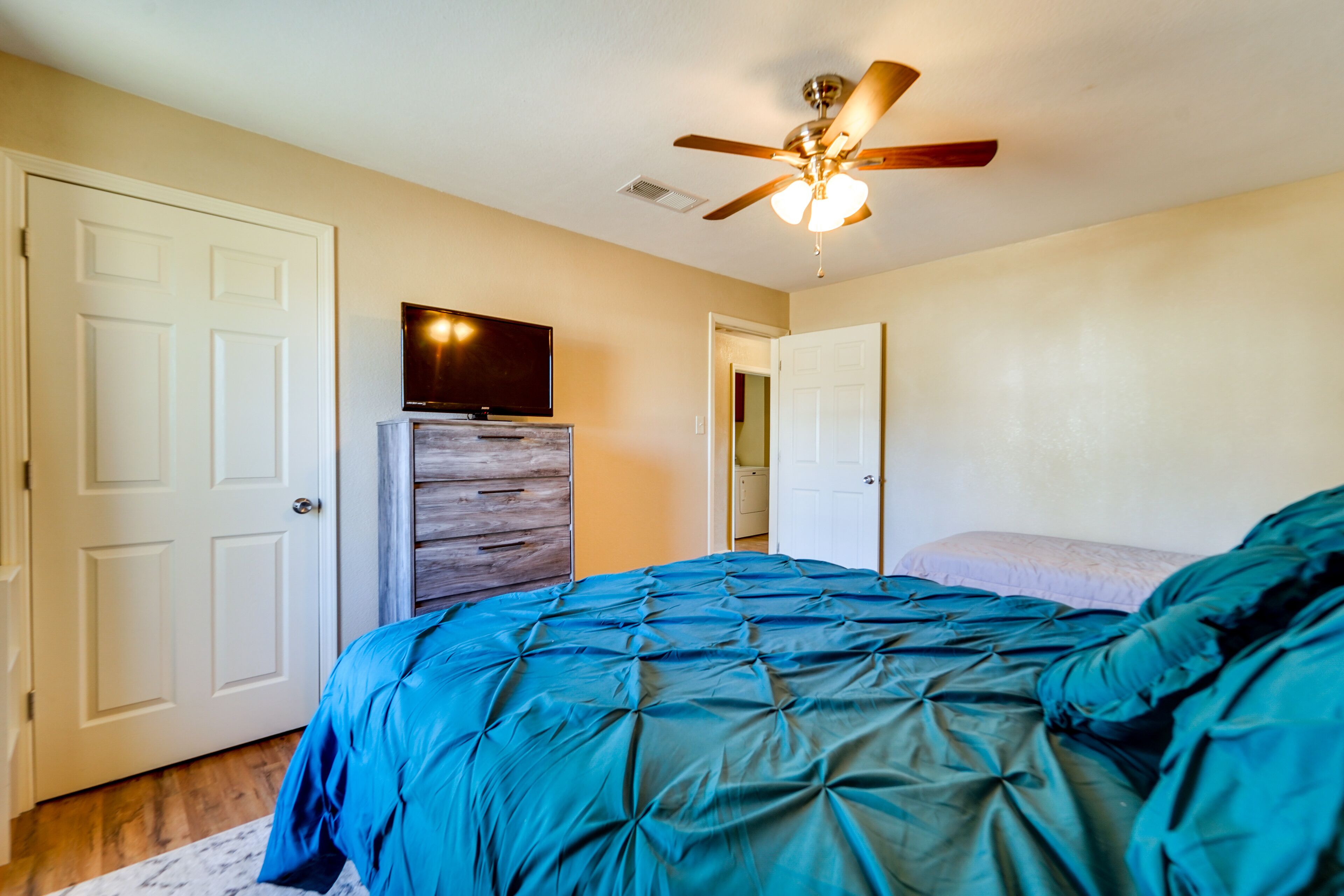 A bedroom with a bed, a ceiling fan, and a television on a wooden cabinet.