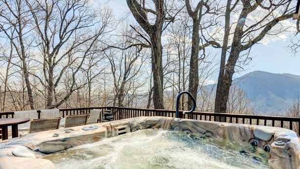 A hot tub surrounded by a wooden deck with chairs, set against a backdrop of leafless trees and mountains. - Hot Tub, Decks & More! Serene Maggie Valley Home (Maggie Valley)