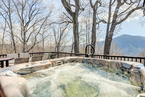 A hot tub surrounded by a wooden deck with chairs, set against a backdrop of leafless trees and mountains. - Hot Tub, Decks & More! Serene Maggie Valley Home (Maggie Valley)