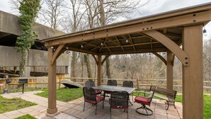 An outdoor patio with a pergola, stone flooring, and metal furniture.