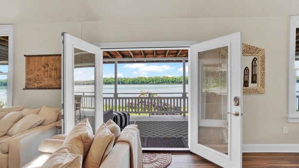 A room with a beige sofa, a glass door leading to a balcony with a view of a lake and trees. - Tuscan River Retreat with Scenic River Views  (York)