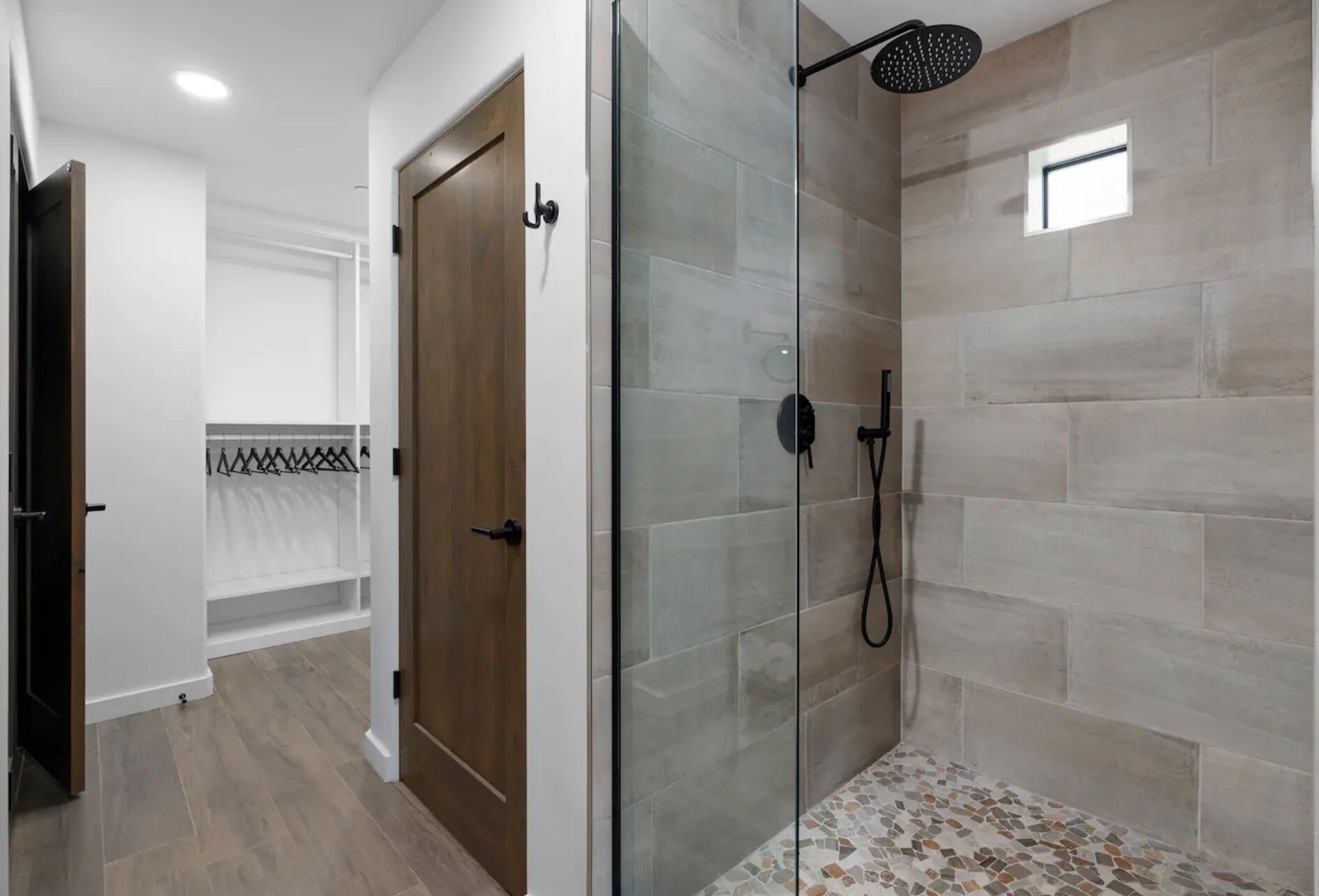 Une salle de bain moderne avec une douche à parois de verre, une porte en bois et un sol carrelé.