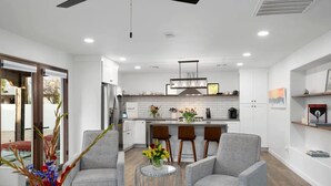 A modern kitchen with white cabinets, a central island with bar stools, and a dining area with grey upholstered chairs.