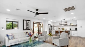 A modern living room with a glass coffee table, grey sofas, and a ceiling fan.
