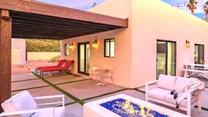 A modern outdoor patio with a fire feature, white furniture, and a covered seating area.