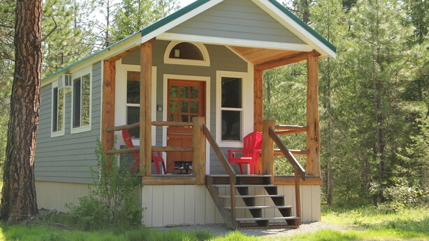 A small cabin with a porch, wooden stairs, and a red chair.