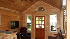 A wooden cabin with a TV, a couch, a chair, and a wooden table.