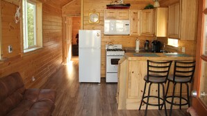 A wooden cabin kitchen with a refrigerator, stove, microwave, and wooden bar stools.
