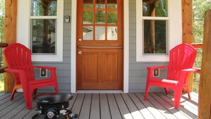 A wooden door with glass panels, flanked by two red chairs on a wooden deck.