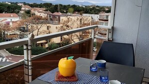 A balcony with a table set for two, a yellow fruit, and a view of a residential area with mountains in the background. - Studio 2 Personnes Proche Plage et Commerces - 2phoe504 (CANET PLAGE)