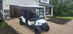 Een golftrolley geparkeerd voor een huis met een overdekte veranda en een stenen muur.