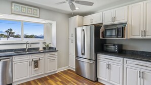 A modern kitchen with white cabinets, stainless steel appliances, a granite countertop, and a wooden floor.