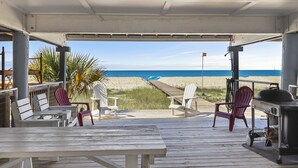 A covered deck with wooden benches and chairs, overlooking a beach.