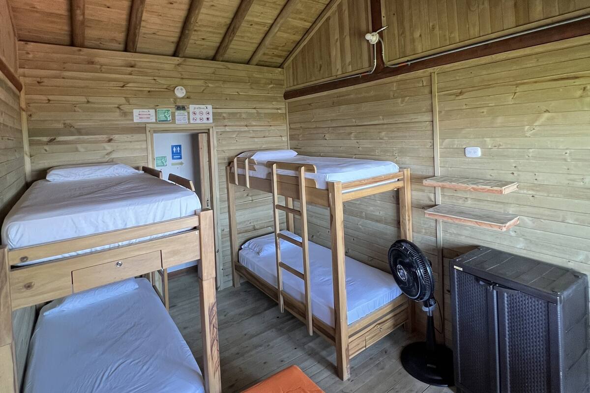 L'intérieur d'une cabane en bois, avec des lits superposés, un ventilateur et un radiateur.