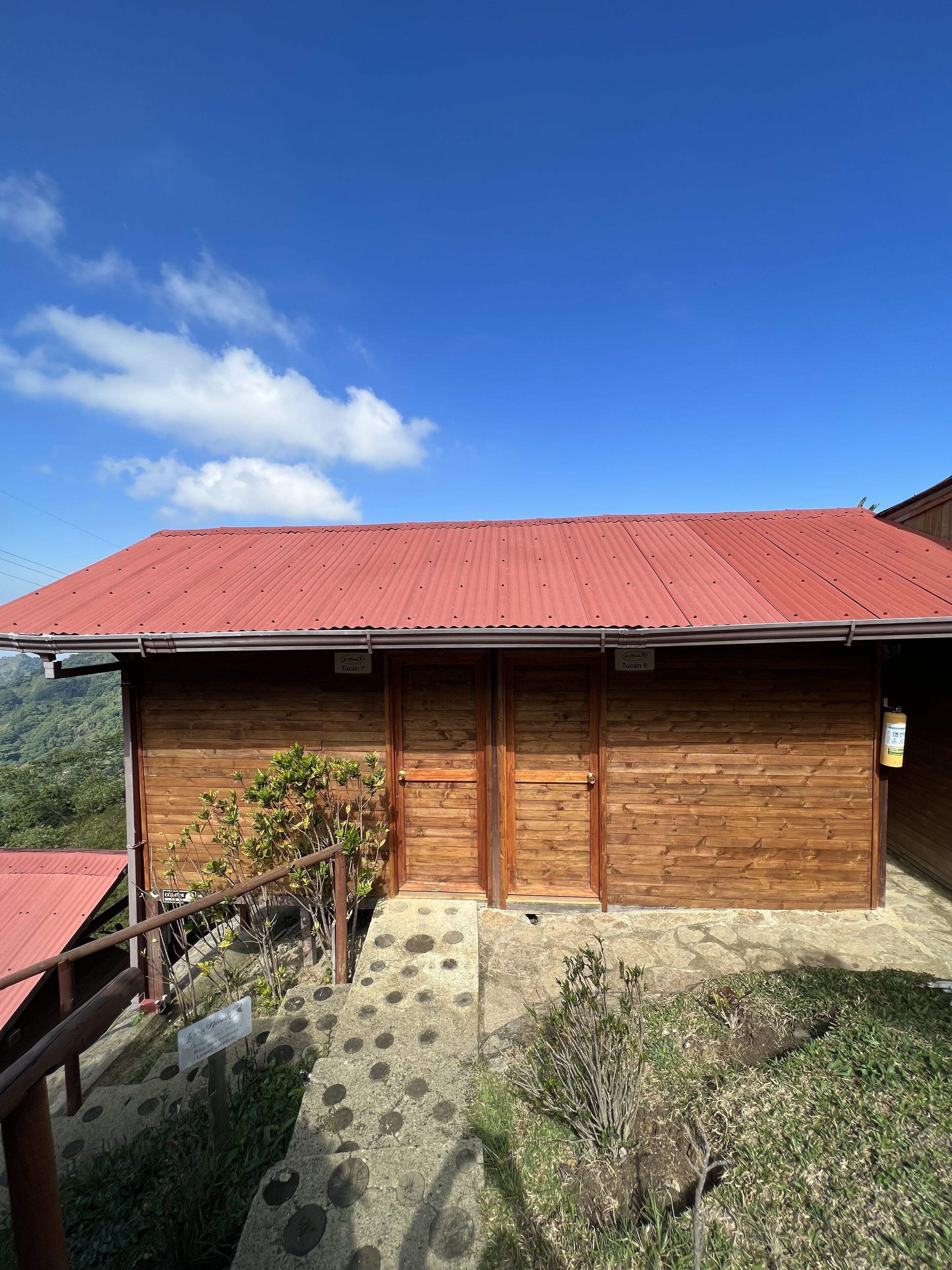 A wooden building with a red roof, a wooden door, and a small garden area with a stone pathway.