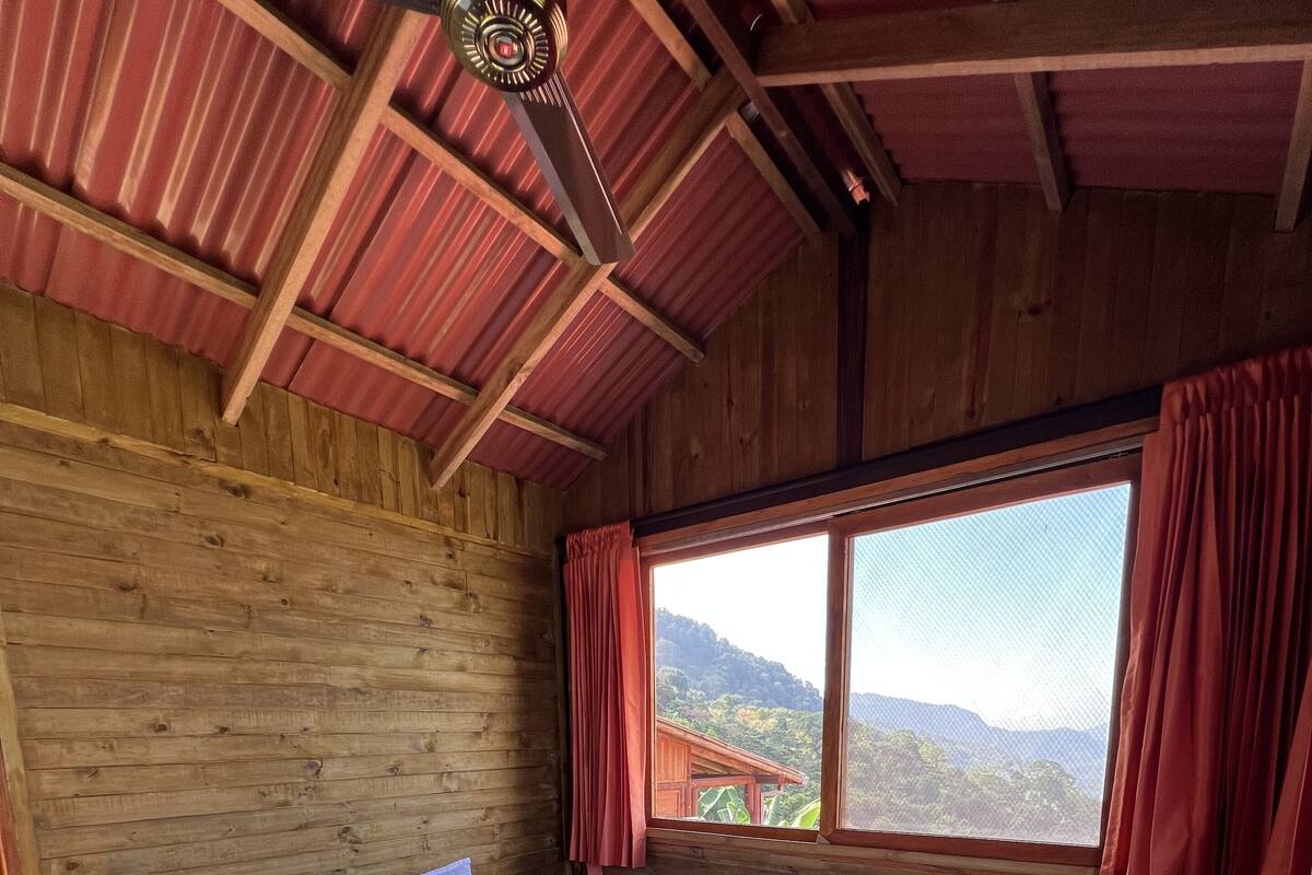 Une pièce de style cabane en bois, avec un lit, une fenêtre avec des rideaux et un ventilateur de plafond.