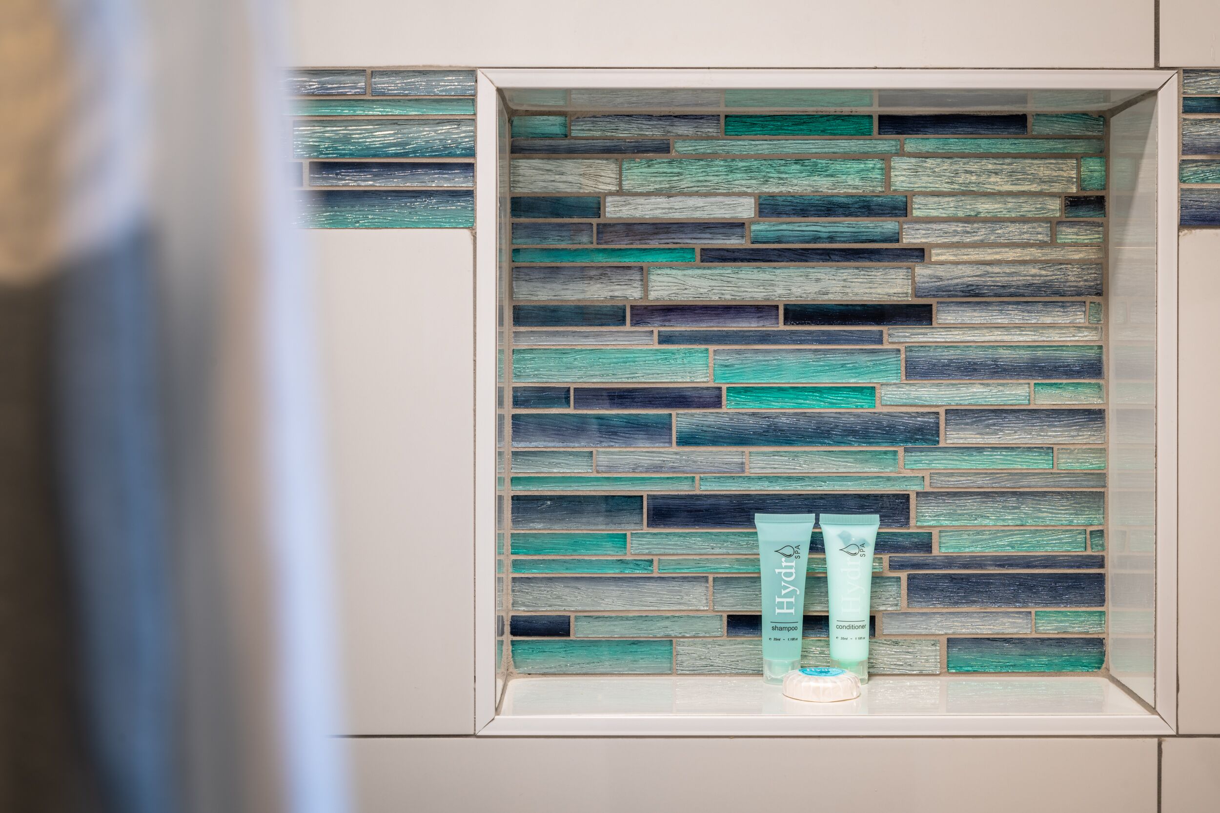 Un baño con pared de azulejos y dos botellas de champú y acondicionador.