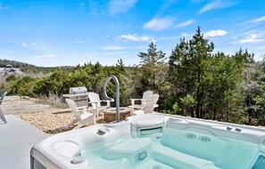 Un bain à remous avec trois sièges et un barbecue, entouré d’arbres et sous un ciel dégagé.
