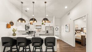 Une cuisine moderne dotée d’un îlot central, de tabourets de bar noirs, d’appareils électroménagers en acier inoxydable et de luminaires suspendus.