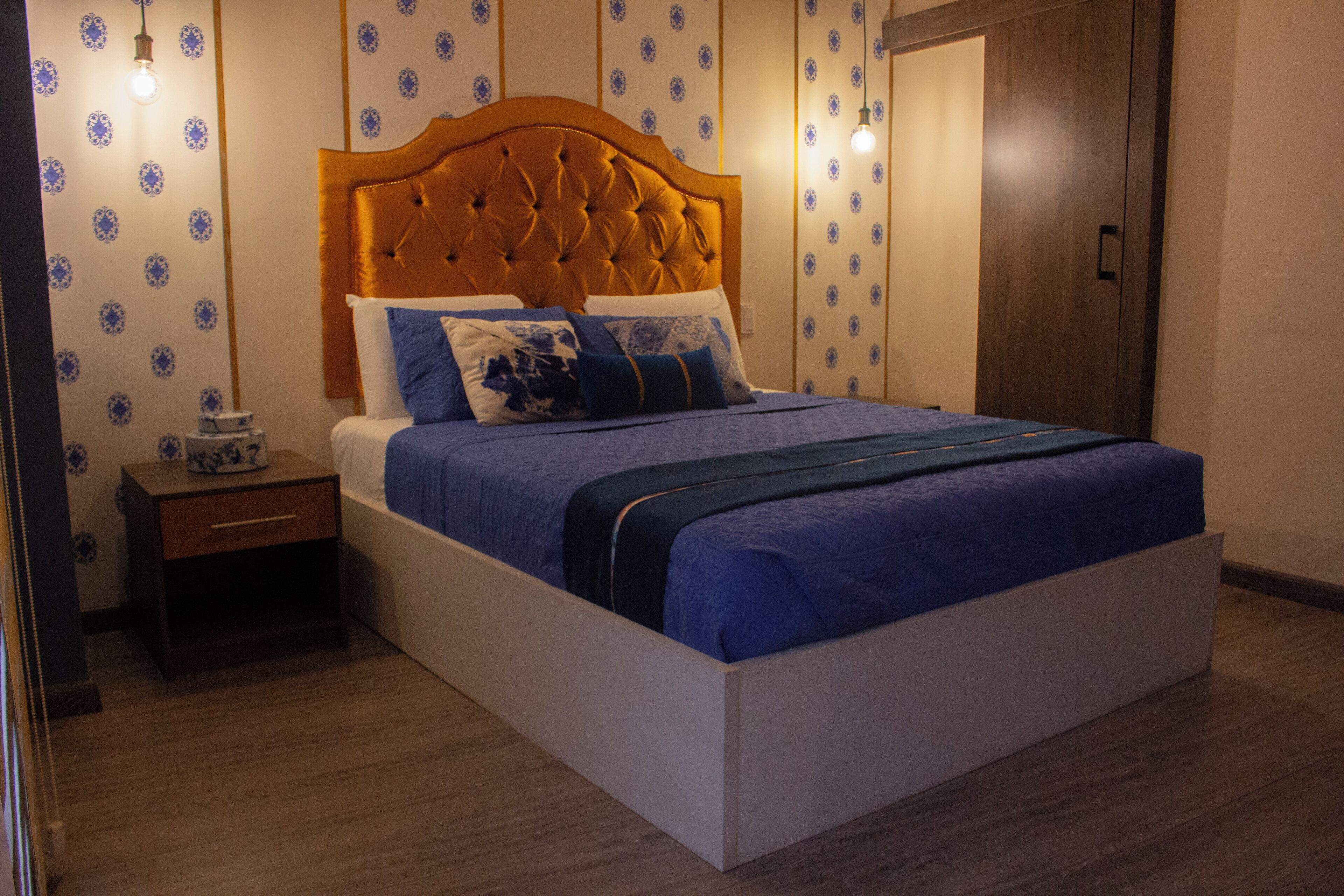 A neatly made bed with a wooden headboard, a bedside table, and patterned wallpaper.