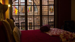 A room with a large window, a bed with a red bedspread, and a chair. - Hotel Boutique La Ronda by Chat Noir (Cuenca)