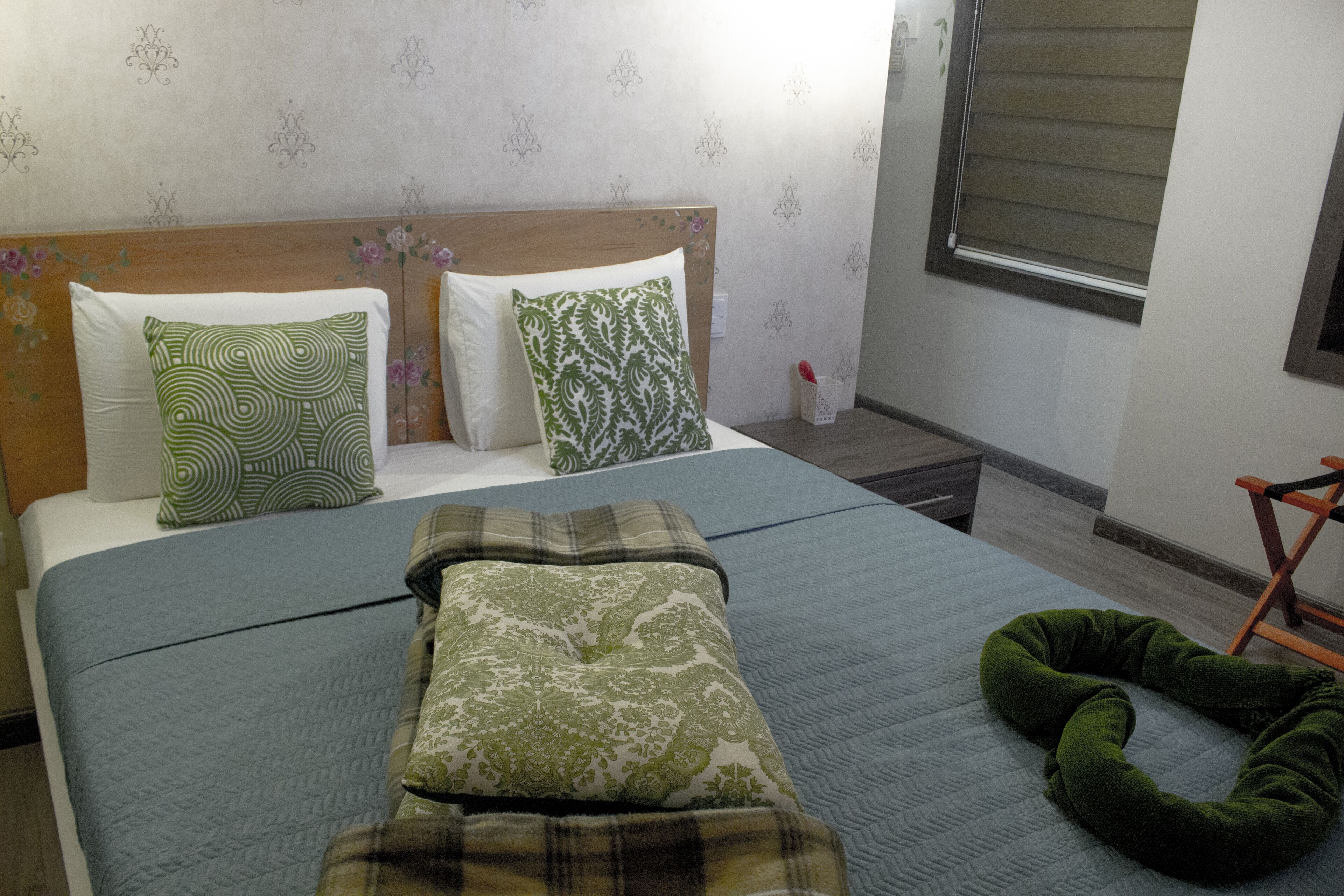Una cama bien hecha con almohadones estampados, un reposacabezas verde y una manta escocesa.