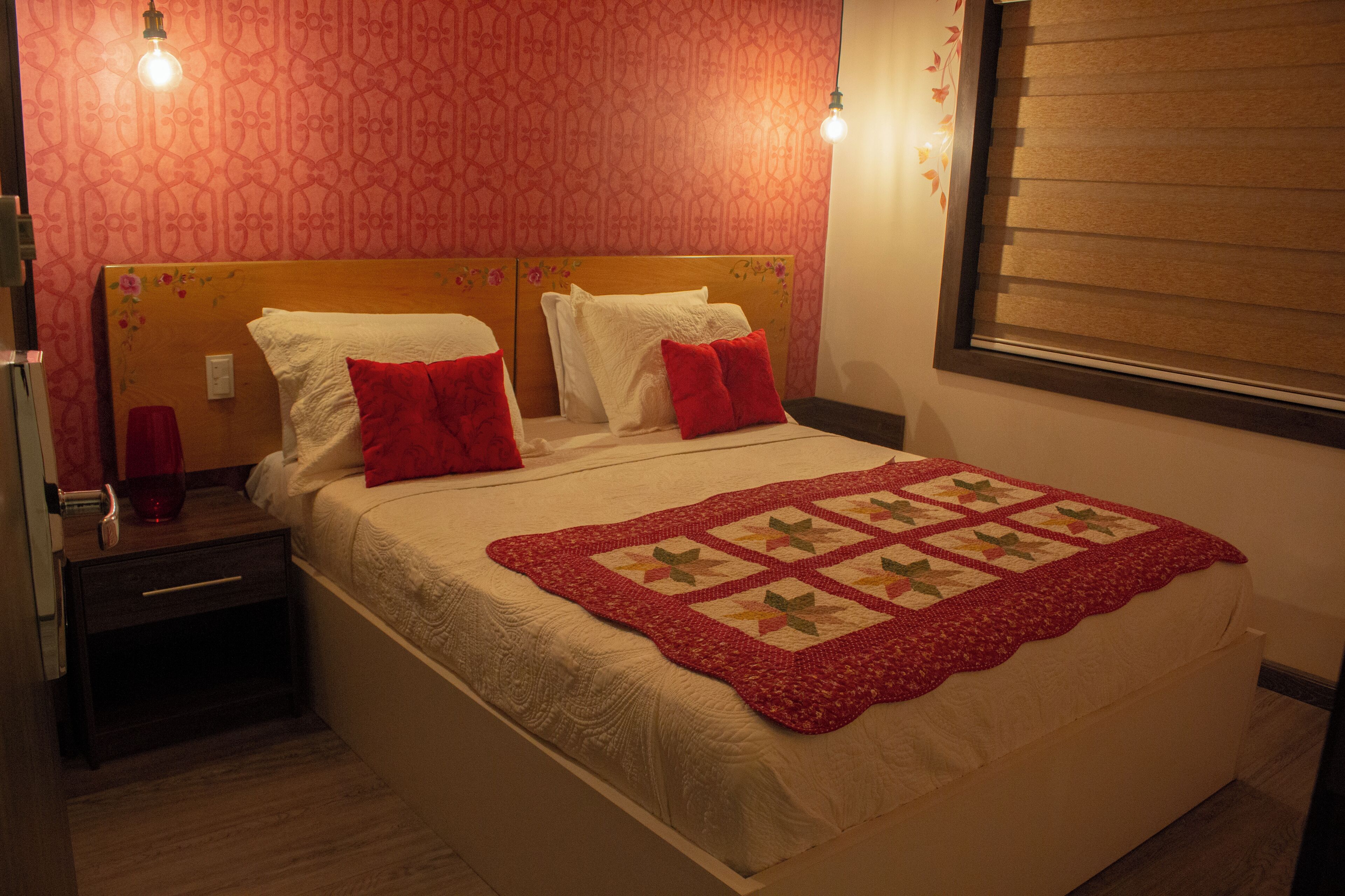 A neatly made bed with a quilt and pillows, a nightstand with a lamp, and a patterned wall.