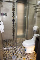 A bathroom with a glass-enclosed shower, a toilet, and patterned floor tiles.