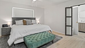 A modern bedroom with a large bed, a green ottoman, a ceiling fan, and a nightstand with a lamp. - Family Friendly, Updated, Charming Home in North Denton (Denton)