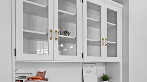 A white cabinet with glass doors and gold handles, a white shelf with a sign, and a basket with items. - Family Friendly, Updated, Charming Home in North Denton (Denton)