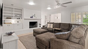 A modern living room with a fireplace, white brick accent wall, and a ceiling fan. - Family Friendly, Updated, Charming Home in North Denton (Denton)