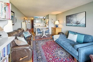 Un salon comprenant un canapé, un divan bleu, une table à manger avec des chaises, un coin cuisine et un tableau accroché au mur.