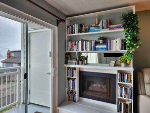 A living room with a fireplace, bookshelves, a door leading outside, and a balcony. - Fun Ocean View Condo - Ground Floor - Fireplace! (Lincoln City)
