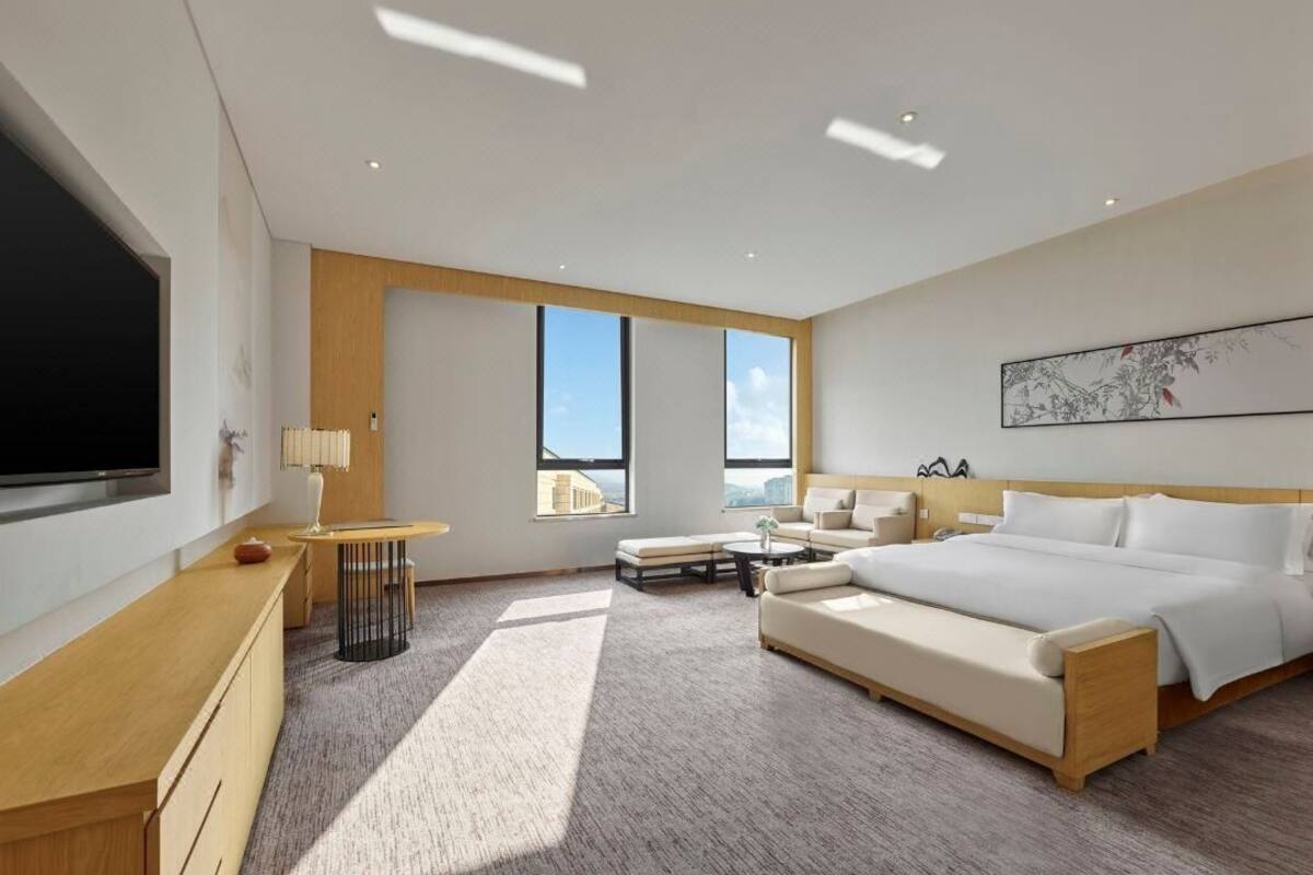 Ein modernes Hotelzimmer mit einem großen Bett, einem Schreibtisch, einem Fernseher und einem Fenster mit Blick auf die Stadt.