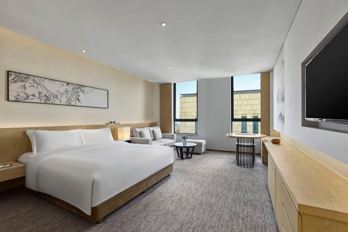 Ein modernes Hotelzimmer mit einem großen Bett, einer Couch, einem kleinen Tisch und einem Fernseher.
