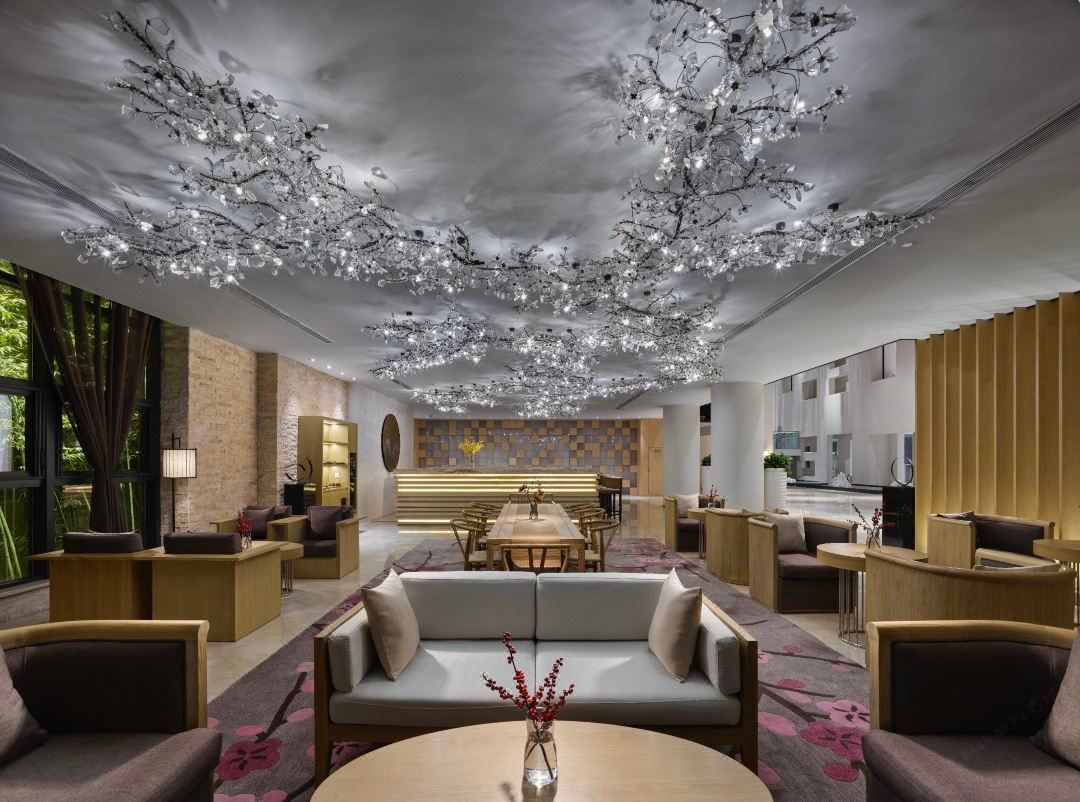 A modern hotel lobby with a central seating area, a reception desk, and a dining area.