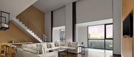 A spacious living area with a large sectional sofa, a coffee table, and a staircase leading to an upper level.