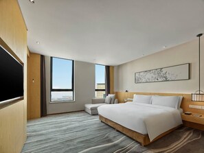 A modern hotel room with a large bed, a flat-screen TV, a sofa, and a large window offering a city view. - Garrya Xian Lintong (Xi'an)