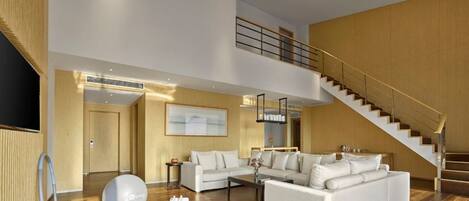A spacious living area with a white sofa set, a coffee table, and a large decorative ball. A staircase with a wooden railing leads to an upper level.