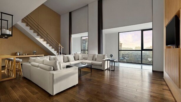 A spacious living area with a large sectional sofa, a coffee table, and a staircase leading to an upper level. - Garrya Xian Lintong (Xi'an)