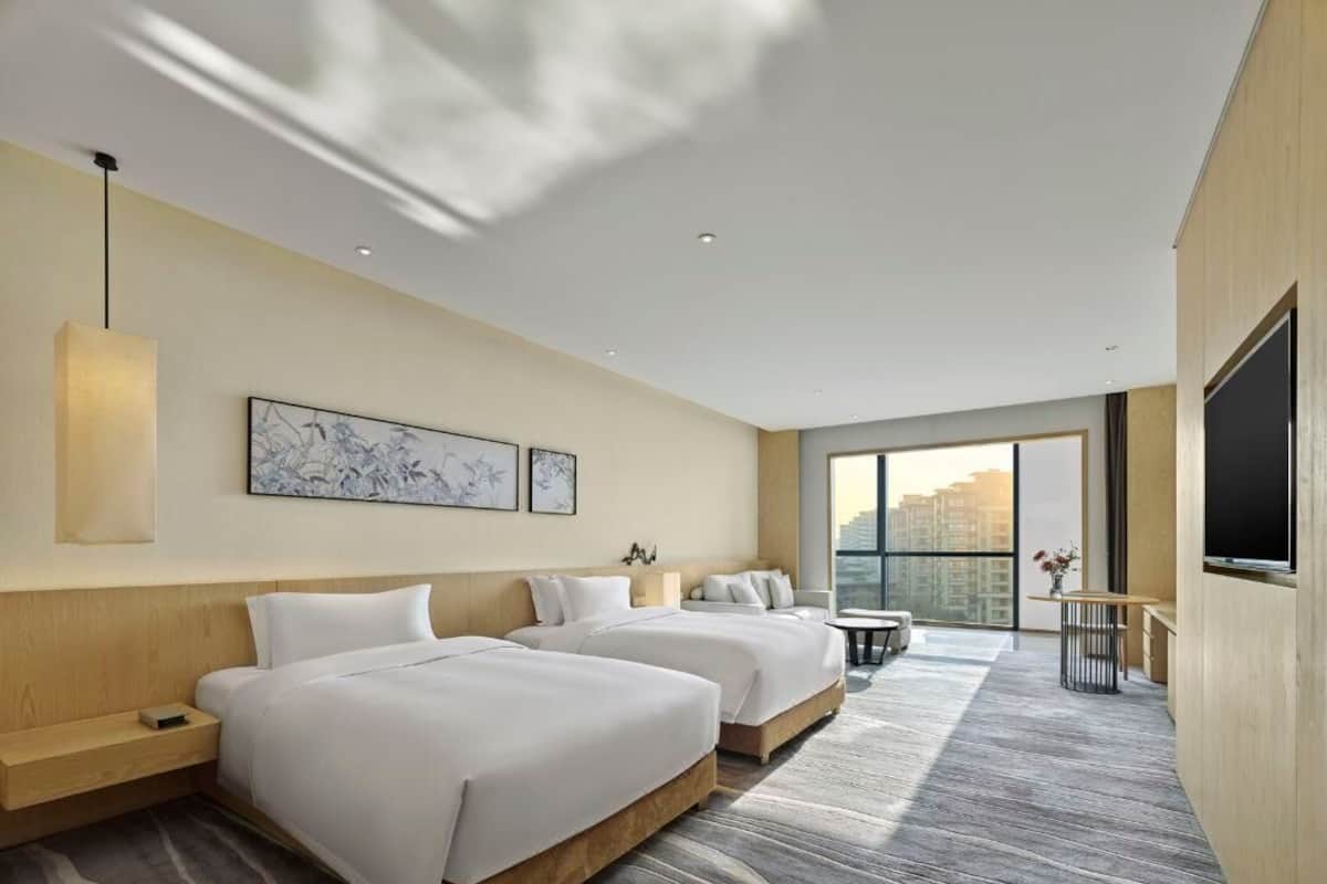 Ein Hotelzimmer mit zwei Betten, einem Fernseher, einem Schreibtisch und einem großen Fenster mit Blick auf die Stadt.