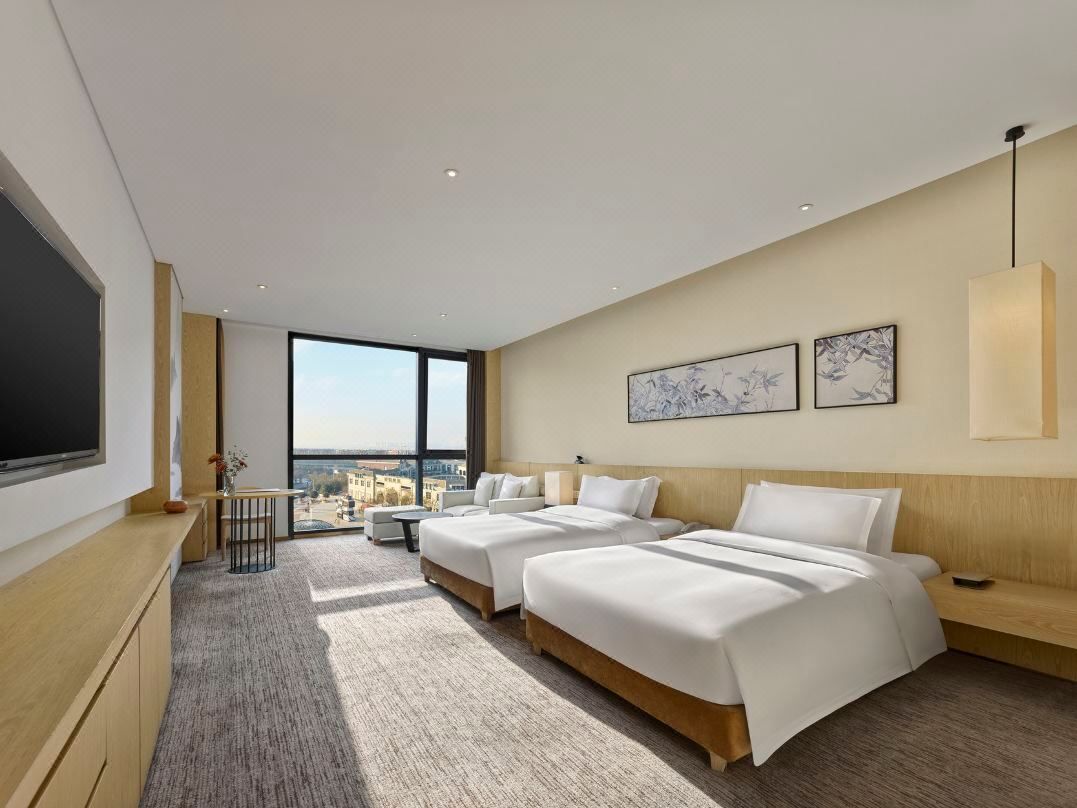 A modern hotel room with two beds, a large window, and a city view.