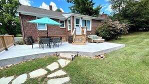 Una casa de maó amb un pati que inclou taula i cadires, una zona de seients a l'aire lliure i un camí de pedra que condueix a la casa.