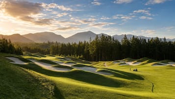 A golf course with sand bunkers, a flagstick, and a person in a golf outfit.