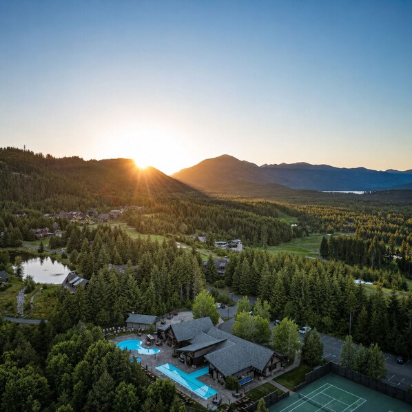A lodge with a swimming pool, tennis court, and forested landscape.
