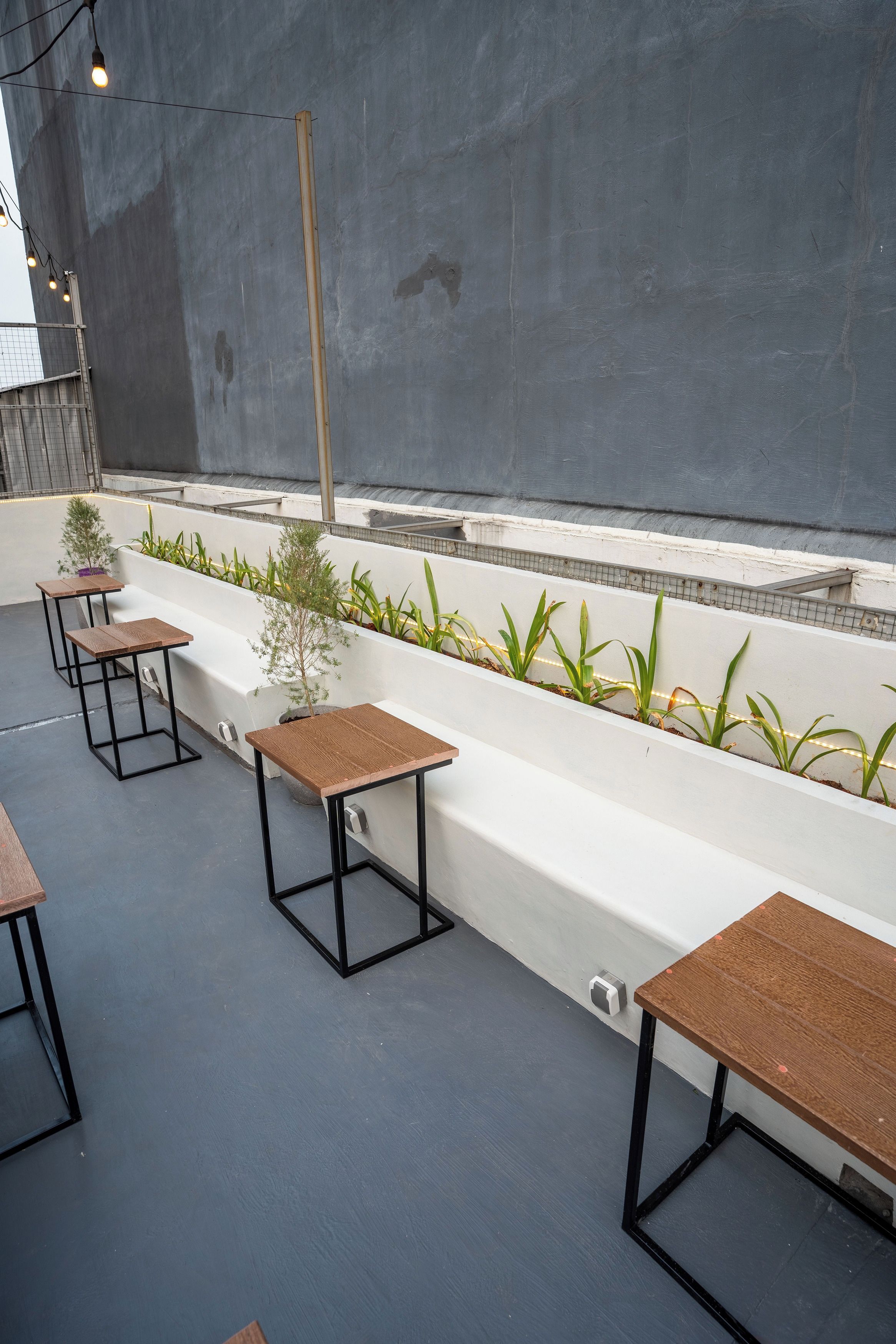 A rooftop terrace with seating areas, a planter with plants, and a grey wall.