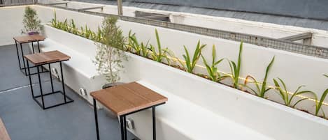 A rooftop terrace with seating areas, a planter with plants, and a grey wall.
